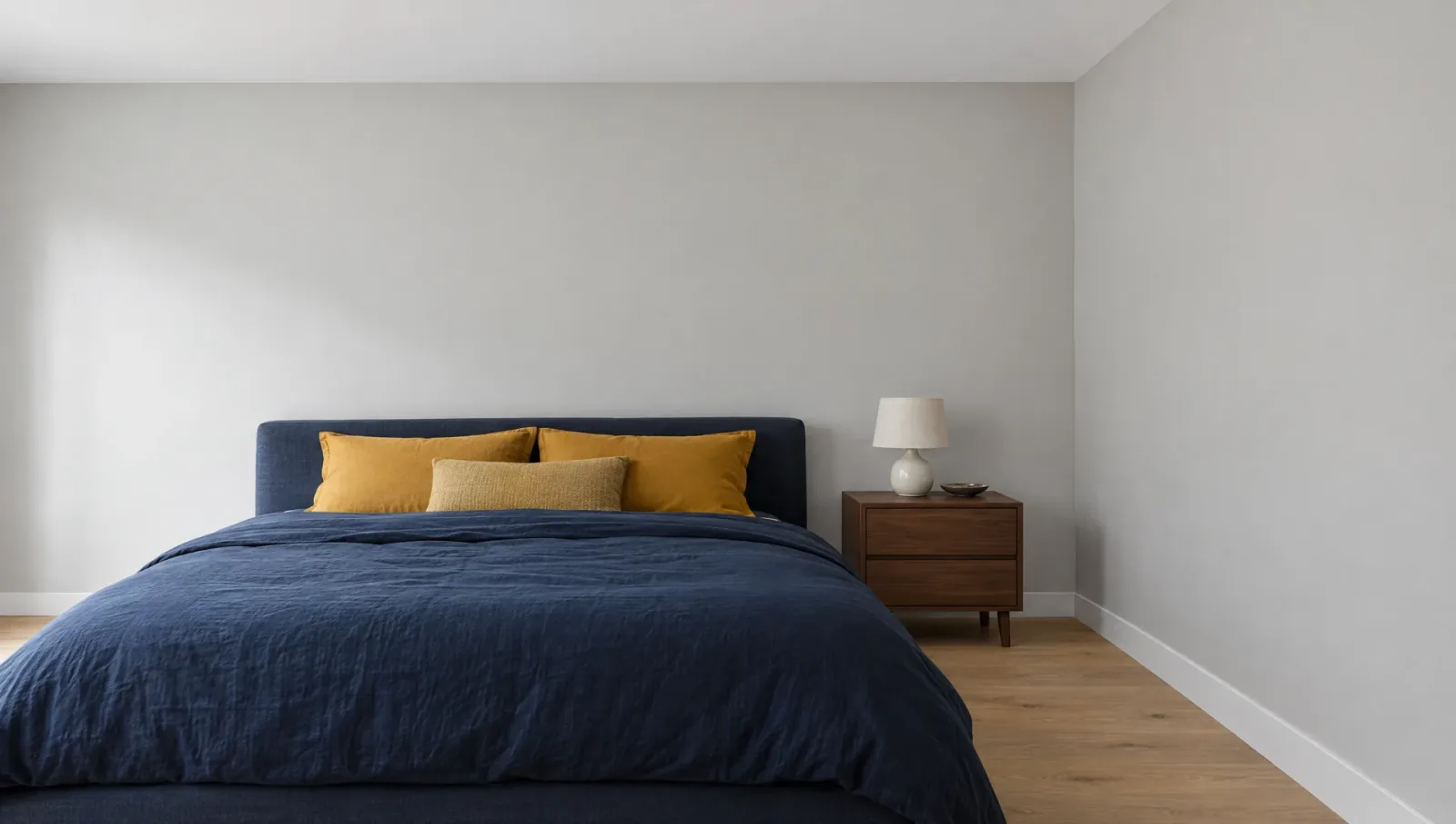 Dormitorio con cama azul, cojines mostaza y velador de nogal